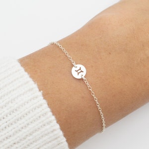 May include: A silver chain bracelet with a circular charm featuring the Gemini zodiac symbol.
