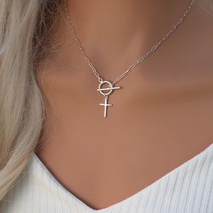 May include: A silver chain necklace with a toggle clasp and a small cross pendant.