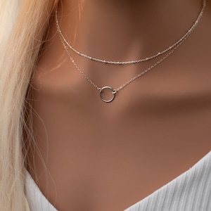 May include: A silver layered necklace with a delicate circle pendant. The necklace is on a mannequin with blonde hair.