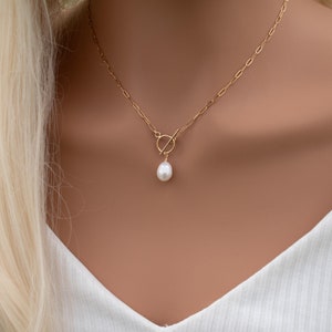 May include: A gold chain necklace with a toggle clasp and a single white pearl pendant.