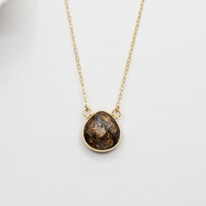 May include: A gold chain necklace with a brown gemstone pendant. The pendant is a faceted, irregular shape.