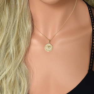 May include: A gold chain necklace with a round pendant featuring a detailed design. The pendant is a circular coin with a raised design.