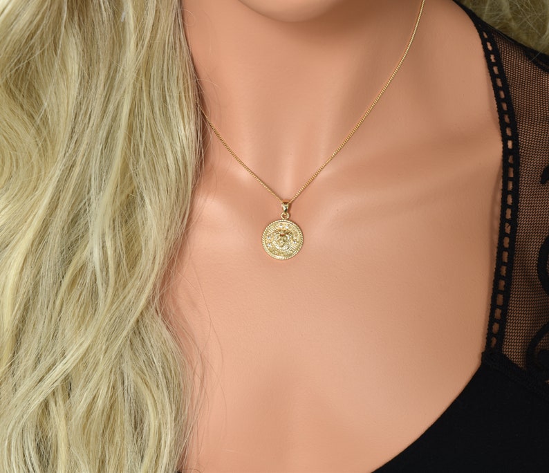 May include: A gold chain necklace with a round pendant featuring a detailed design. The pendant is a circular coin with a raised design.