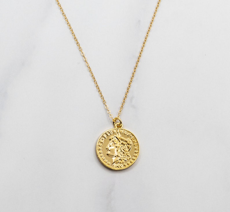 May include: A gold chain necklace with a gold coin pendant featuring a profile of a woman with a crown.