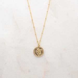 May include: A gold chain necklace with a round gold coin pendant featuring a detailed profile of a woman's face.
