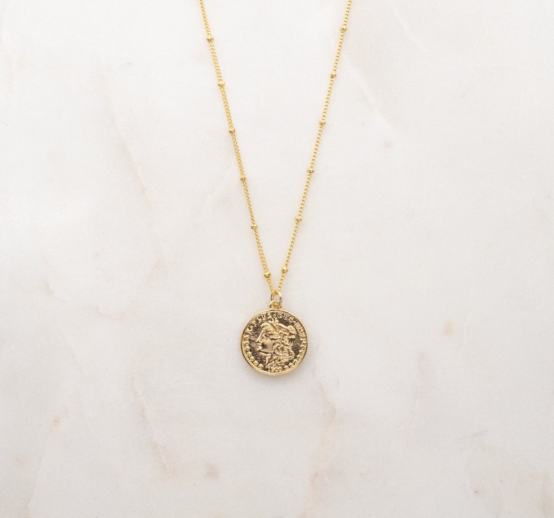 May include: A gold chain necklace with a round gold coin pendant featuring a detailed profile of a woman's face.