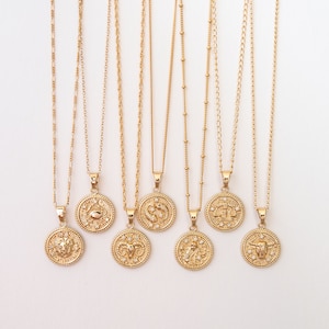 May include: Eight gold necklaces with zodiac signs pendants. Each pendant features a different zodiac symbol with a gold finish and small clear crystals. The necklaces are on a white background.