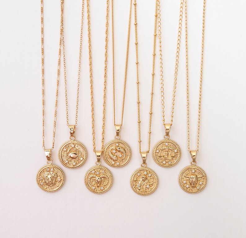May include: Eight gold necklaces with zodiac signs pendants. Each pendant features a different zodiac symbol with a gold finish and small clear crystals. The necklaces are on a white background.