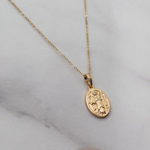 May include: A gold chain necklace with a gold oval pendant featuring a detailed image of an angel with wings.
