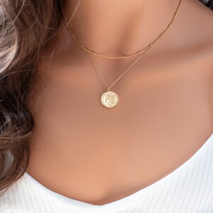 May include: A gold layered necklace with a coin pendant. The coin has a detailed design and is on a delicate chain.