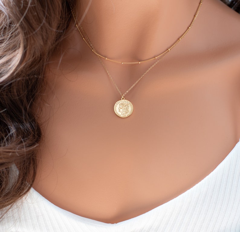May include: A gold layered necklace with a coin pendant. The coin has a detailed design and is on a delicate chain.