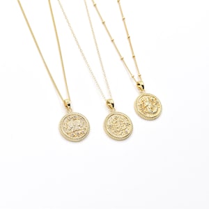 May include: Three gold necklaces with round pendants featuring intricate designs and small clear stones. The pendants are all different, but they have a similar style.