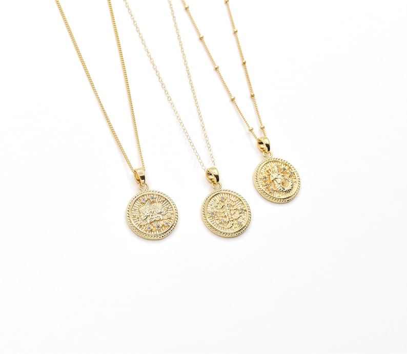May include: Three gold necklaces with round pendants featuring intricate designs and small clear stones. The pendants are all different, but they have a similar style.