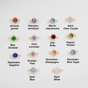 May include: Twelve gold charms with different coloured gemstones, each representing a different month of the year. The charms are arranged in four rows of three. The gemstones are: garnet, amethyst, aquamarine, clear crystal, emerald, lavender, ruby, peridot, sapphire, pink, champagne, and blue topaz. The last two charms are opal, one blue and one white.