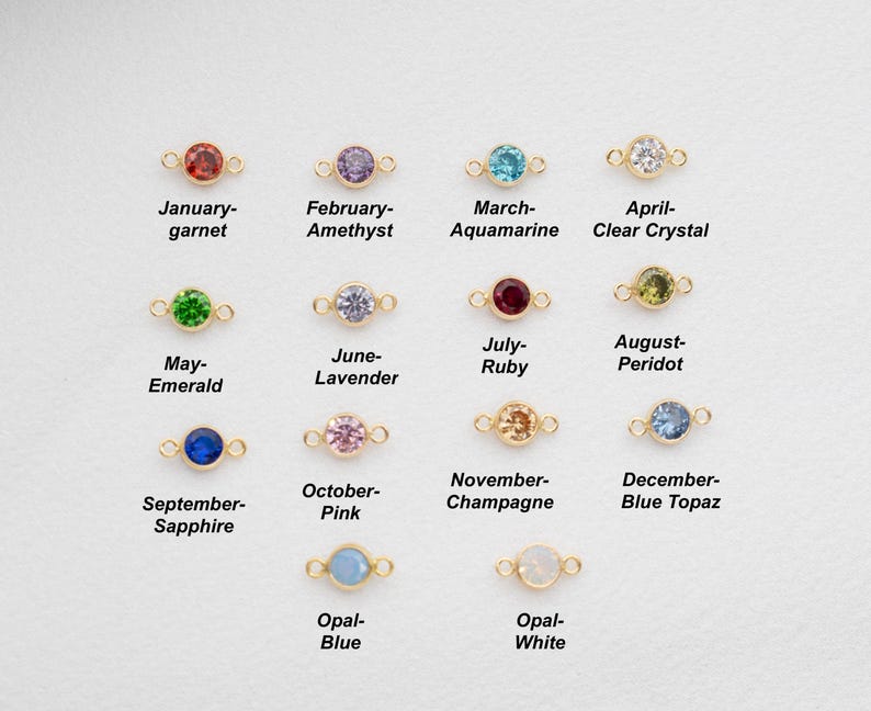 May include: Twelve gold charms with different coloured gemstones, each representing a different month of the year. The charms are arranged in four rows of three. The gemstones are: garnet, amethyst, aquamarine, clear crystal, emerald, lavender, ruby, peridot, sapphire, pink, champagne, and blue topaz. The last two charms are opal, one blue and one white.