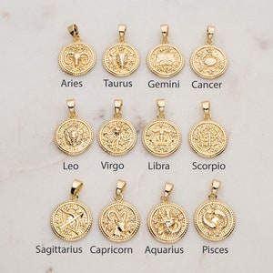 May include: Twelve gold zodiac pendants with a white crystal accent. Each pendant features a different zodiac symbol, including Aries, Taurus, Gemini, Cancer, Leo, Virgo, Libra, Scorpio, Sagittarius, Capricorn, Aquarius, and Pisces.