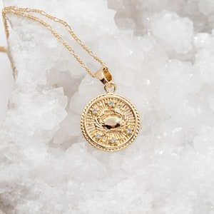 May include: Gold necklace with a round pendant featuring a crab design and small clear stones. The pendant is on a delicate chain.