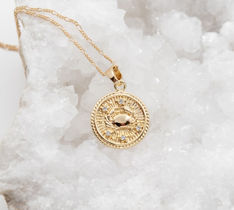 May include: Gold necklace with a round pendant featuring a crab design and small clear stones. The pendant is on a delicate chain.