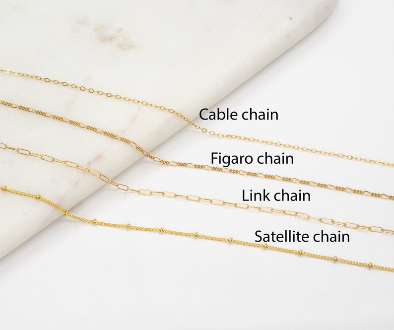 May include: Four gold chains of different styles: cable chain, figaro chain, link chain, and satellite chain. The chains are laid out horizontally on a white surface.