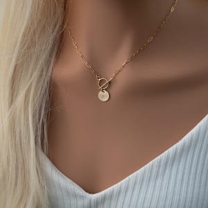 May include: A gold chain necklace with a toggle clasp and a round pendant featuring an eye design.