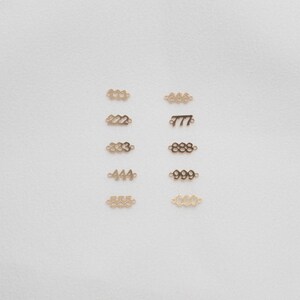 May include: A set of ten gold-coloured metal number charms, each charm features a different number from 111 to 666. The charms are arranged in two rows of five, on a white background.