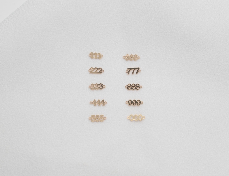 May include: A set of ten gold-coloured metal number charms, each charm features a different number from 111 to 666. The charms are arranged in two rows of five, on a white background.