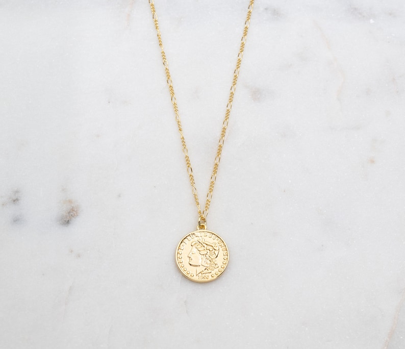 May include: A gold chain necklace with a gold coin pendant featuring a profile of a woman's face. The coin has a raised rim and intricate details.