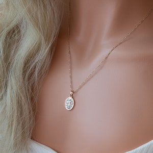 May include: A gold chain necklace with a small round pendant featuring a detailed design. The pendant is hanging on a delicate chain.