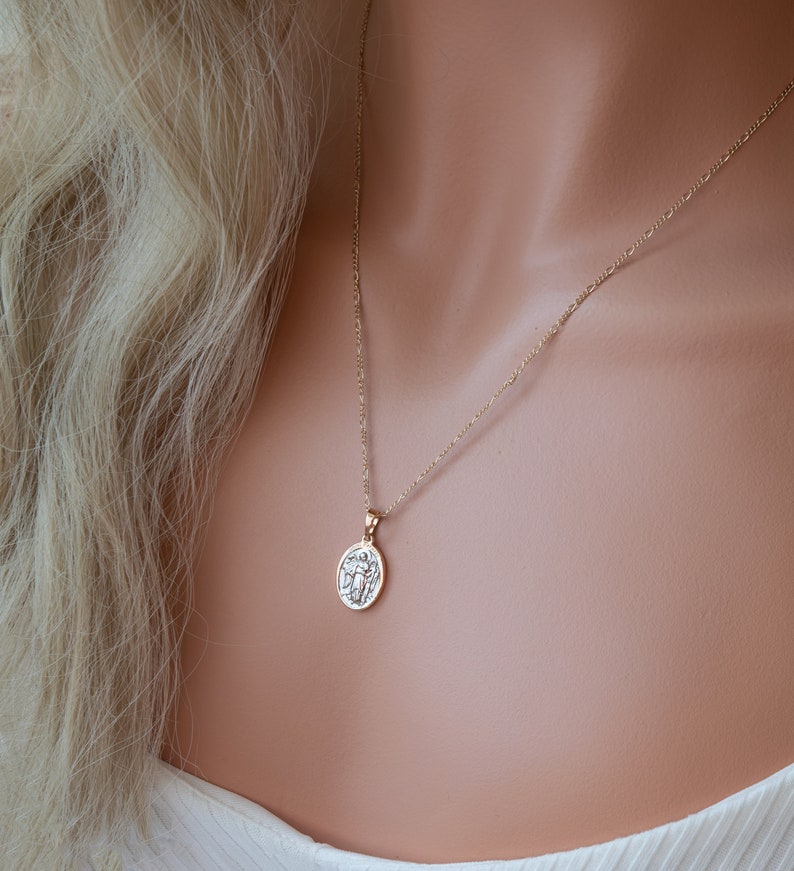May include: A gold chain necklace with a small round pendant featuring a detailed design. The pendant is hanging on a delicate chain.