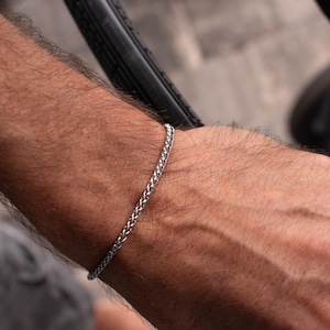 May include: A silver chain bracelet on a person's wrist.