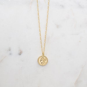 May include: A gold chain necklace with a gold coin pendant featuring a profile of a woman's face.