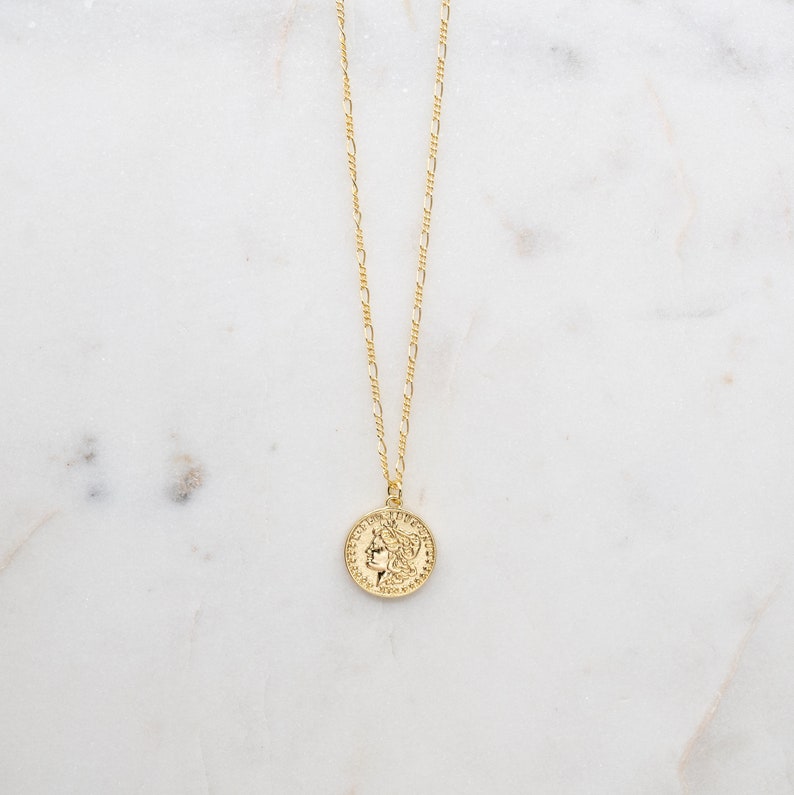May include: A gold chain necklace with a gold coin pendant featuring a profile of a woman's face.
