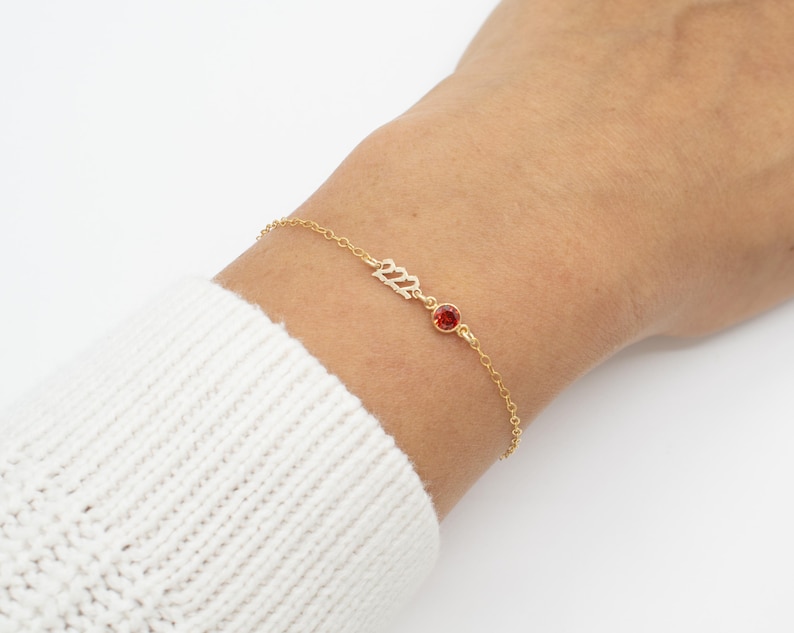 May include: A gold chain bracelet with a red gemstone and the number 2022 in gold lettering.
