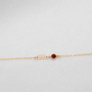 May include: A delicate gold chain necklace with a small red gemstone and the number "22" charm.