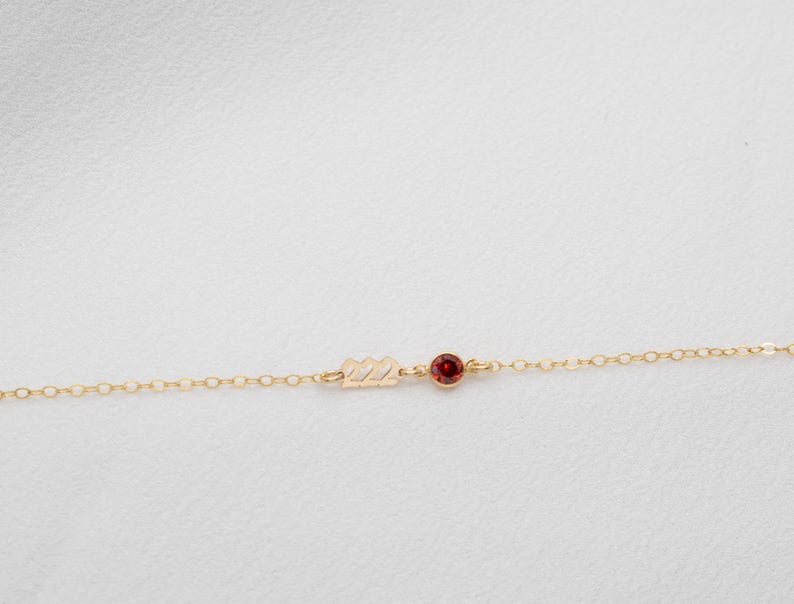 May include: A delicate gold chain necklace with a small red gemstone and the number "22" charm.