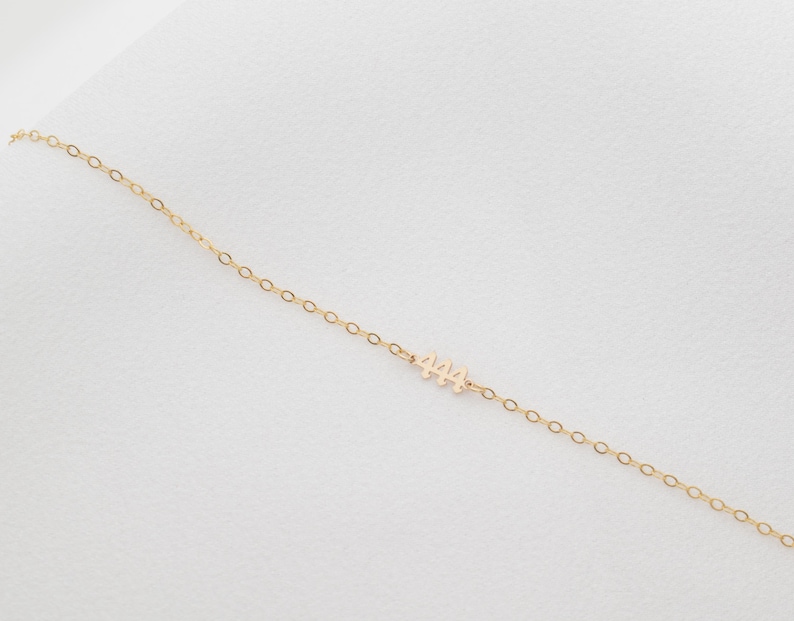 May include: A delicate gold chain necklace with a small pendant featuring the number "444".