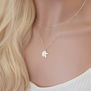 May include: A silver chain necklace with a small cross pendant. The necklace is layered with a delicate silver chain.