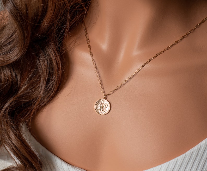 May include: A gold chain necklace with a textured gold coin pendant.