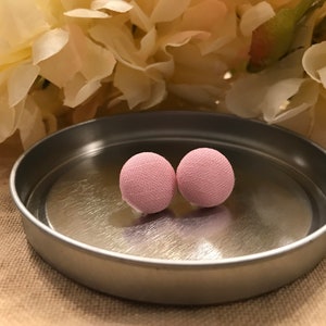 Pode incluir: Um par de brincos de botão de tecido rosa. Os brincos estão em uma bandeja prateada.
