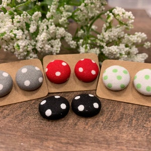 Puede incluir: Seis pares de pendientes de botón de tela con lunares blancos sobre fondos de colores diferentes. Los colores son gris, rojo, verde y negro.