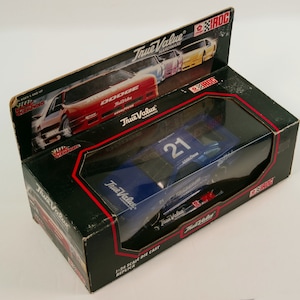May include: A 1/24 scale die-cast replica of a blue Dodge Daytona stock car with the number 21 and the True Value Hardware logo. The car is in a black box with a clear plastic window.