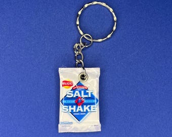 May include: A white keychain shaped like a bag of Walker's Salt & Shake potato chips. The bag has blue and red accents and the text "Salt & Shake" in a blue box.