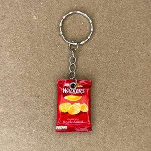 May include: A red and white bag of Walkers crisps with the text "Classically Ready Salted" on the front. The bag is attached to a silver keychain.
