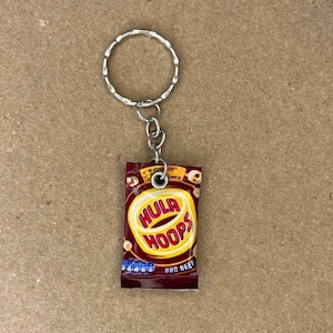 May include: A novelty keychain with a miniature packet of Hula Hoops crisps. The packet is red with the Hula Hoops logo in yellow and white. The keychain has a silver ring and chain.