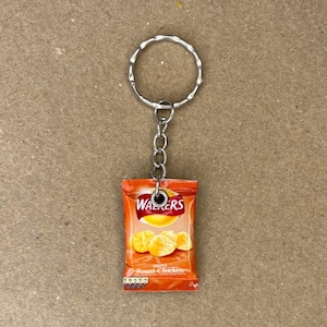 May include: A keychain shaped like a bag of Walkers crisps, featuring a red and orange bag with the text "Walkers" and "Roast Chicken" printed on it. The bag contains three yellow potato chips.