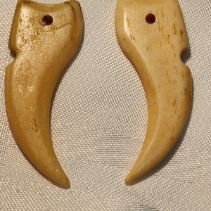 May include: Two carved bone pendants shaped like claws, each with a small hole for hanging.