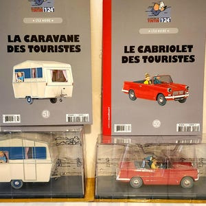 Peut inclure: Deux objets de collection Tintin : une maquette de caravane blanche et une voiture d&eacute;capotable rouge, chacune dans un pr&eacute;sentoir transparent. La caravane est tir&eacute;e de "La Caravane des Touristes" et la voiture de "Le Cabriolet des Touristes".