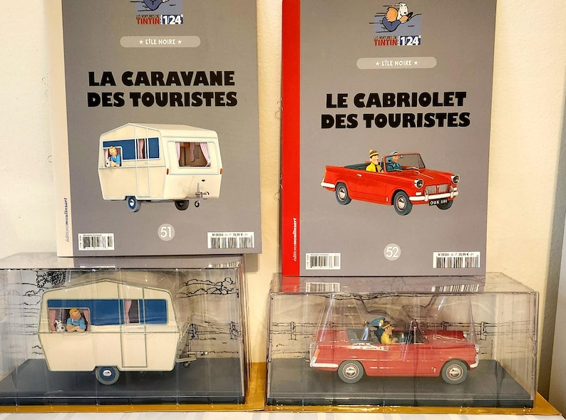 Peut inclure: Deux objets de collection Tintin : une maquette de caravane blanche et une voiture d&eacute;capotable rouge, chacune dans un pr&eacute;sentoir transparent. La caravane est tir&eacute;e de "La Caravane des Touristes" et la voiture de "Le Cabriolet des Touristes".