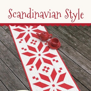 May include: Red and white table runner with a Scandinavian snowflake design. The runner is made of fabric with white polka dots on a red background. The text "This & That" and "Original Quilt Patterns by Sherri K. Falls" is on the runner. The number "#312" is in the bottom right corner.