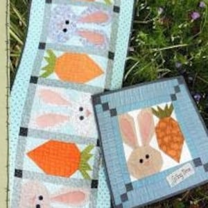 May include: A blue and white patchwork quilt with a bunny and carrot design. The quilt is made up of squares and rectangles. The quilt is called "Springtime Bunny #209".